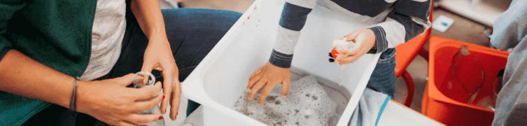 A young child and their teacher play with a sensory bin in their classroom.