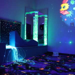 A room with glow in the dark space themed carpet is dimly lit up by a fibreoptic lamp and wall projection.