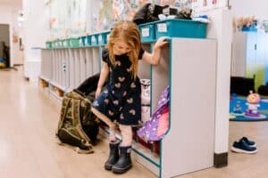 A young girl steps into her winter boots outside of her school locker