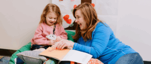 A young girl reads a book with her class aide