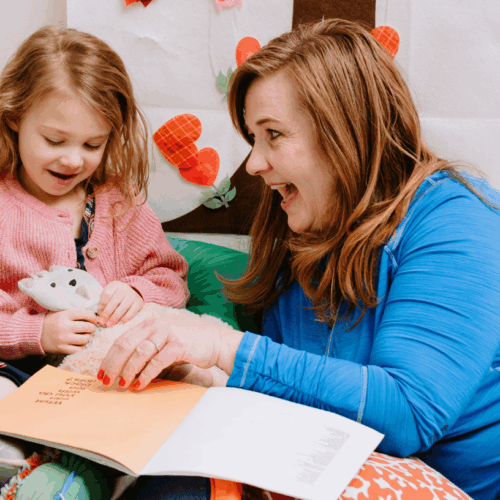 A young girl reads a book with her class aide