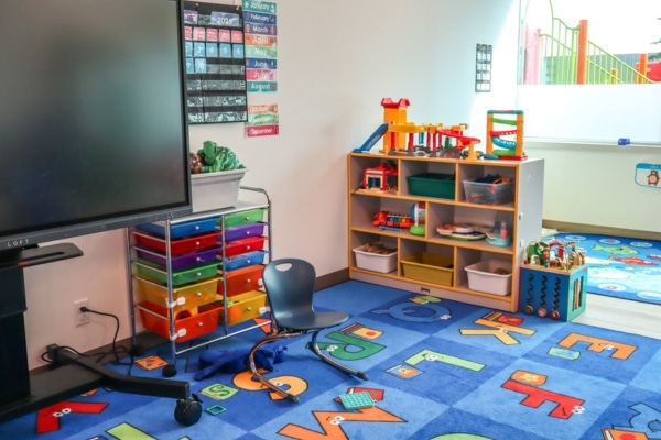 Early childhood classroom with colorful rugs, toys, and learning materials.