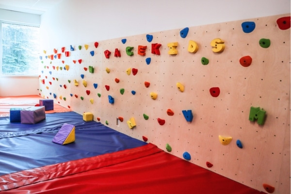 Indoor children’s climbing wall with colorful holds and padded flooring.