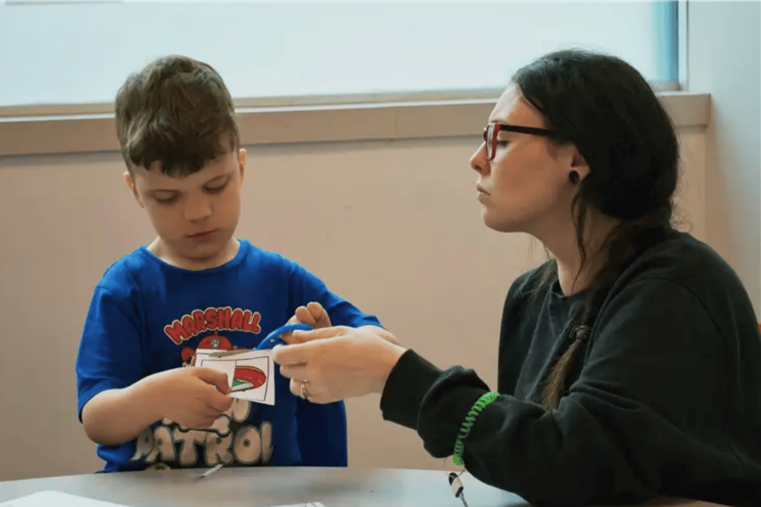 Young boy with diverse needs in blue shirt with a teacher working through picture activity