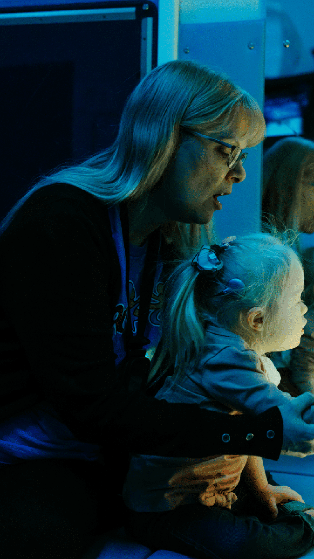 A young girl and her class aide place their hands on a bubble tube in a dark sensory room